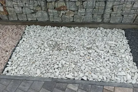 Biały grys, czyli drobne, łamane kamienie, tworzy jasną powierzchnię obok gabionów i ciemniejszego kamienia.