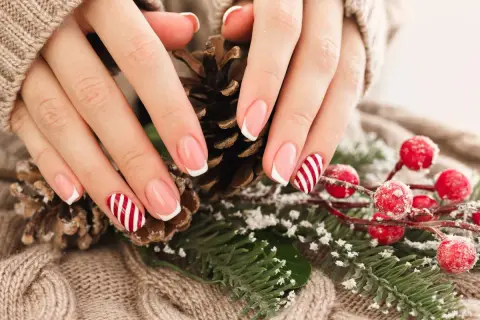 Jasne paznokcie świąteczne z motywem cukierków i francuskim manicure, otoczone szyszkami i gałązkami ostrokrzewu.