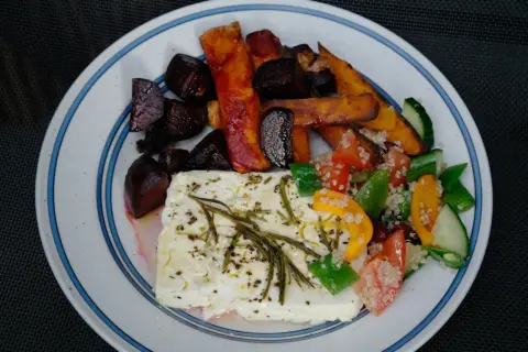 En tallrik med ugnsbakade rödbetor, sötpotatisstavar och en stor bit fetaost i ugn, toppad med örter. Serveras med en fräsch sallad.