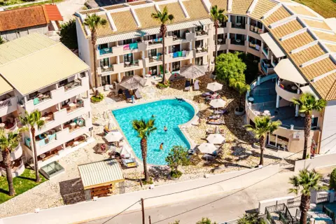 Widok z lotu ptaka na basen i budynki hotelowe. Wiele osób odpoczywa przy basenie. Warto sprawdzić caretta island hotel opinie przed rezerwacją.