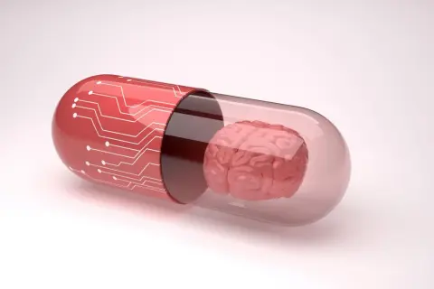 Czerwona kapsułka z obwodem drukowanym zawiera mózg, symbolizując potencjalne leki, np. inhibitory MAO, wpływające na funkcje poznawcze.