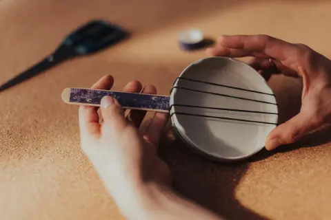 Dziecko tworzy proste instrumenty muzyczne: ukulele z talerzyka i gumek.