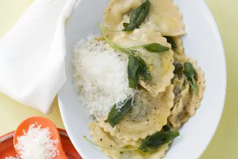 Ravioli mit Spinat-Ricotta-Füllung, Salbeiblättern und geriebenem Parmesan auf einem Teller.