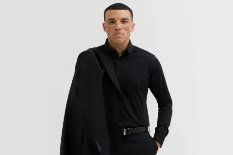 Mężczyzna w czarnym garniturze, z marynarką na ramieniu. Elegancki, czarny pasek do garnituru podkreśla jego styl.