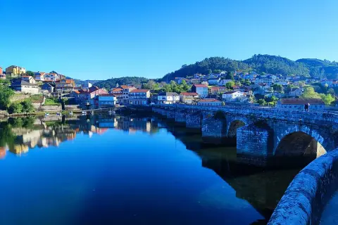 Puente de piedra en Ponte Sampaio, con casas reflejándose en el río azul bajo un cielo despejado.