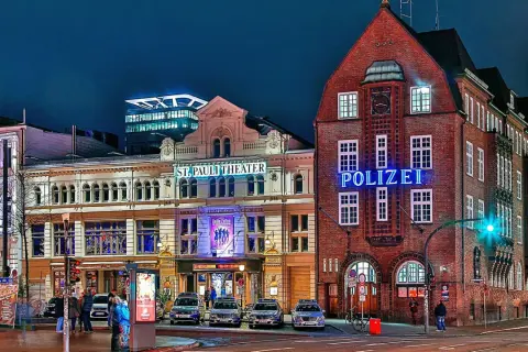 Polizeigebäude und St. Pauli Theater in Hamburg bei Nacht, mit leuchtenden Schildern und Autos.