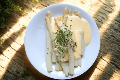 En tallrik med vit sparris, täckt av en krämig sås och toppad med färska groddar. En härlig vårmåltid.