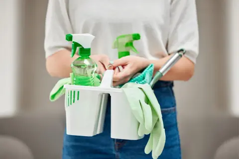 Persona con kit de limpieza: guantes, botellas rociadoras y paños. Las funciones de un auxiliar de limpieza son variadas.