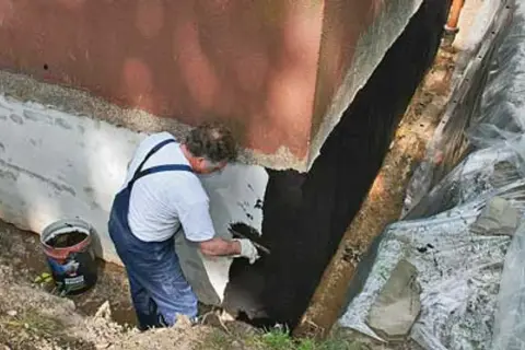 Mann trägt Bitumenanstrich innen auf die Kellerwand auf.