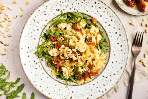 Farfalle-Nudelsalat mit Rucola, getrockneten Tomaten, Pinienkernen und Mozzarella. Ein mediterraner Genuss!