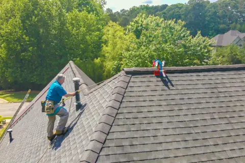 A roofer demonstrates how to shingle a steep roof, using safety gear and a ladder.