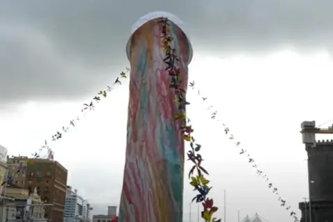 Un'installazione colorata, alta e decorata con festoni di fiori. Si immagina di poter toccare il naso di Pulcinella.