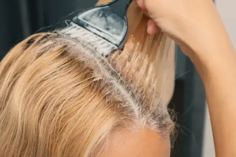 Aplikacja produktu do rozjaśniania włosów na blond. Pędzel równomiernie rozprowadza mieszankę na pasmach.