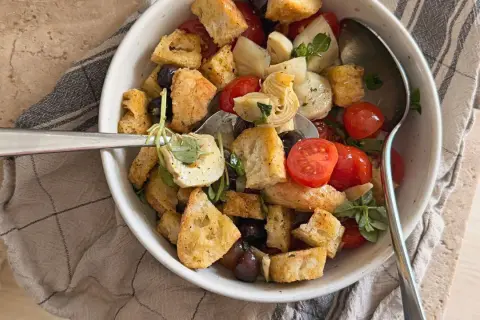 Herzhafter Brotsalat mit Roggenbrot, Kirschtomaten, Oliven und Artischockenherzen, garniert mit frischen Kräutern.