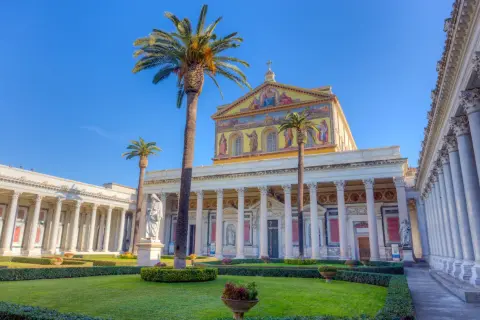 Giardino curato davanti alla Basilica San Paolo, con palme alte e statue.