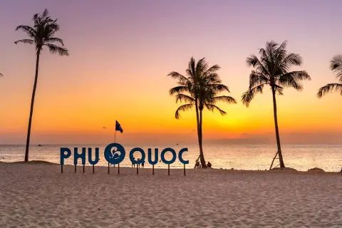 Zachód słońca na plaży Phu Quoc, Wietnam. Palmy i napis "PHU QUOC" na tle pomarańczowego nieba.