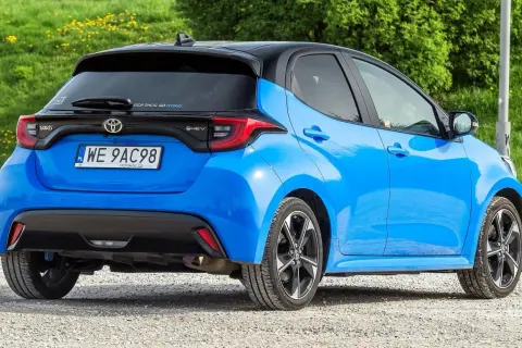 Niebieski Toyota Yaris IV z czarnym dachem, zaparkowany na żwirowej drodze, z zielonym tłem.