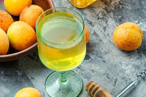Frische Aprikosen und ein Glas goldener Likör – die Zutaten, um Mirabellenschnaps selber zu machen.