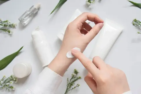 Eine Hand testet eine weiße Creme, umgeben von Pflegeprodukten und zarten Blüten. CI 45410.