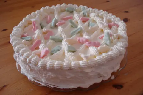 En vit gräddtårta dekorerad med rosa, gröna och vita Ahlgrens bilar. Perfekt för en festlig stund!