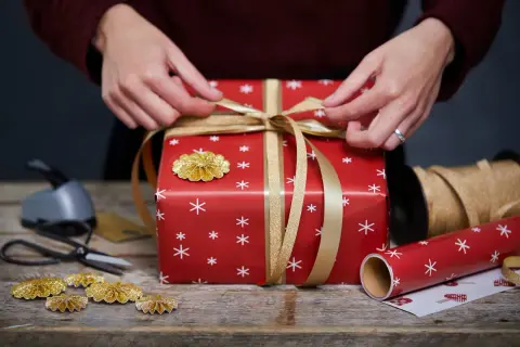 Här är några presentinslagningstips: en röd present med vita snöflingor, gyllene band och dekorationer.