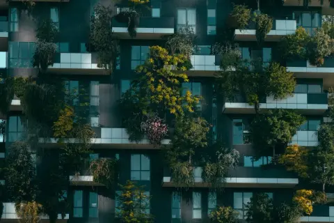 Edificio moderno con balcones repletos de vegetación, un ejemplo de sostenibilidad en la construcción que integra la naturaleza en la vida urbana.