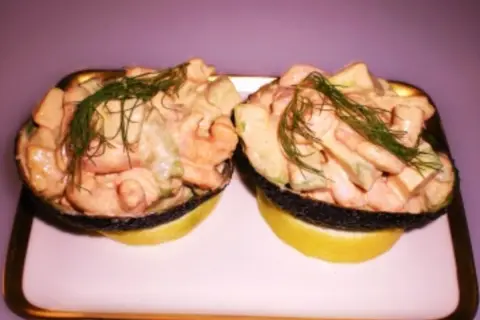 Zwei Avocadohälften gefüllt mit einem cremigen Krabbencocktail mit Avocado und Dill garniert, serviert auf Zitronenscheiben.