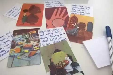 Karty z ilustracjami i notatki z hasłami: "dixit pomysły na hasła", uczta, rycerz, dzieciństwo, para grająca w szachy.