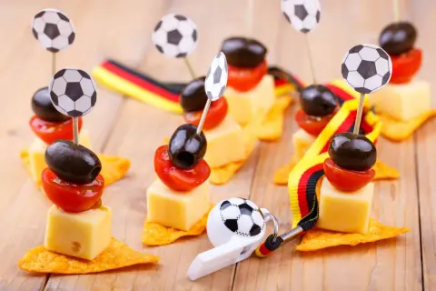 Décoration foot à faire soi même : brochettes de fromage, tomates et olives sur chips, ornées de mini ballons et de rubans aux couleurs allemandes.