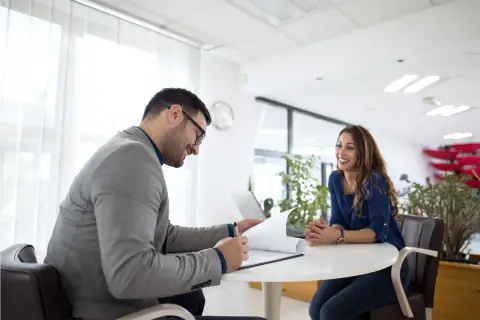 Uomo in giacca grigia firma documenti, donna sorride. Potrebbe essere un colloquio o una discussione su un nuovo progetto di job rotation.