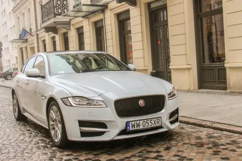 Biały Jaguar XF 3.0 Diesel na brukowanej ulicy przed kamienicą.