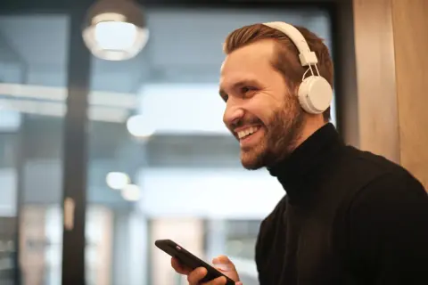 Uśmiechnięty mężczyzna w słuchawkach bezprzewodowych trzyma telefon, pokazując, jak podłączyć słuchawki bezprzewodowe do telefonu.