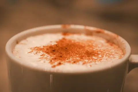 Une tasse blanche remplie d'une boisson crémeuse, saupoudrée de cannelle. Une parfaite composition chai latte pour un moment de détente.