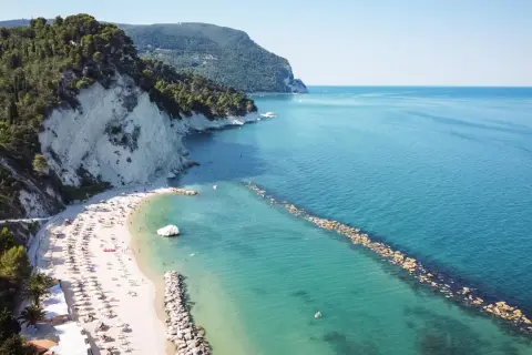 Spiaggia di Marina Palmense con scogliere bianche, mare azzurro e ombrelloni colorati.