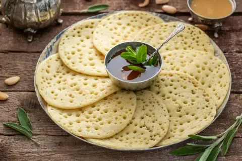 Une assiette de crêpes mille trous dorées, garnie d'une coupelle de miel et de menthe fraîche. Parfait pour un petit-déjeuner gourmand.
