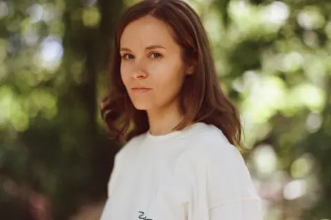 Hania Rani Esja, artystka o hipnotyzującym spojrzeniu, w białej bluzie na tle zieleni.