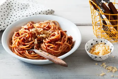 Ein Teller Spaghetti Bolognese, ein Klassiker unter den spaghetti rezepte, mit geriebenem Käse bestreut. Daneben eine Schale mit extra Käse.