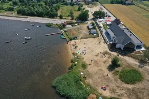 Słoneczny dzień nad zalewem Cedzyna. Ludzie odpoczywają na plaży, pływają i żeglują.