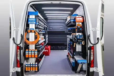 Interior de un autobús camperizado en España, organizado con estanterías y herramientas.