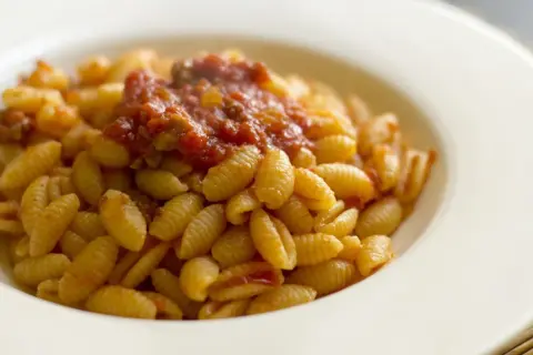 Malloreddus alla campidanese, pasta sarda con sugo di pomodoro e salsiccia, serviti in un piatto bianco.