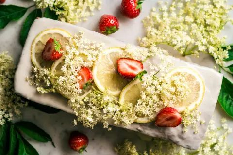 Zarte Holunderblüten, Zitronenscheiben und Erdbeeren zieren ein Gericht, das an einen sommerlichen Holunderkuchen erinnert.