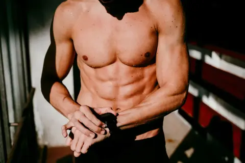 Ein Mann mit einem definierten Sixpack und nasser Haut blickt auf seine Sportuhr.