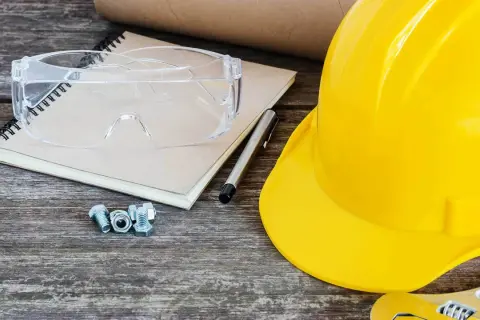 Żółty kask, okulary ochronne, śruby i notatnik leżą na drewnianym stole. Kto przechowuje dziennik budowy po zakończeniu budowy?