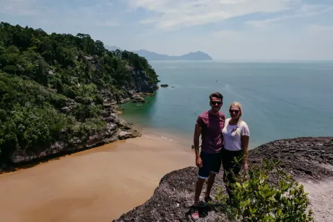 Ein Paar genießt die Aussicht auf eine tropische Bucht mit Sandstrand und Dschungel. Tolle Malaysia Urlaub Erfahrungen!