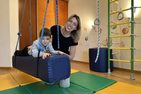 Kobieta i chłopiec w sali terapeutycznej z huśtawką i drabinką.