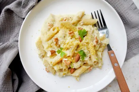 Penne z kremowym sosem z kalafiora, orzechami i natką pietruszki. Pyszny makaron z kalafiorem na białym talerzu.