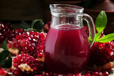 Sok z granatu w ciąży to zdrowy wybór. Na zdjęciu dzbanek z rubinowym sokiem i świeże granaty.