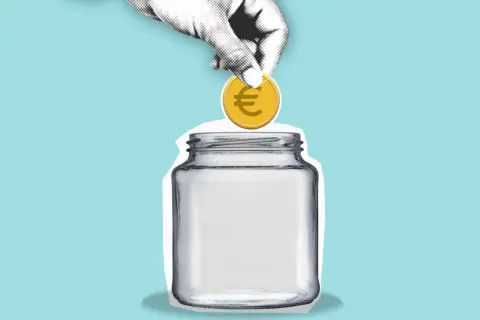 Eine Hand wirft eine Münze mit Euro-Symbol in ein leeres Glas. Sparen für den hauskauf steuer absetzen.