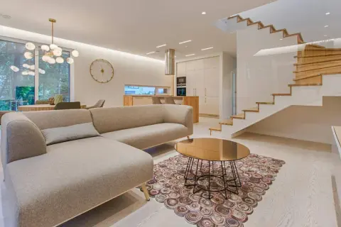 Elegantes ideas de interiores de casas: sofá moderno, mesa de centro dorada, alfombra circular y escaleras de madera flotantes.