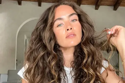 Mujer con un espectacular pelo rizado castaño, con reflejos dorados, acariciando un mechón.